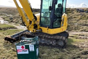 A compact 250-litre Fuel Proof Fuelcube diesel tank sits beside a yellow mini-excavator on a British moor