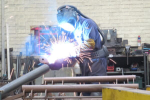 A welder fabricates fuel tank parts in a fly of bright sparks